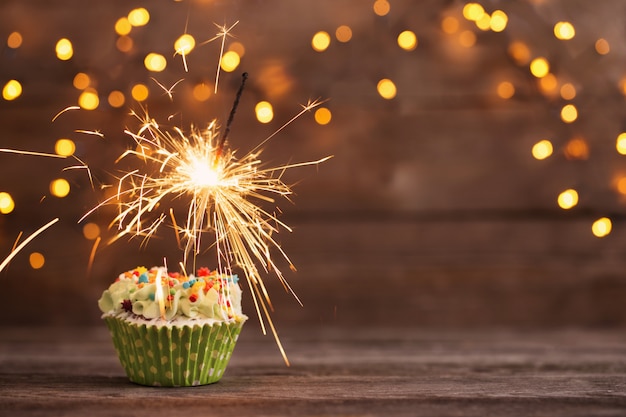 Cupcake with sparkler on old wooden table