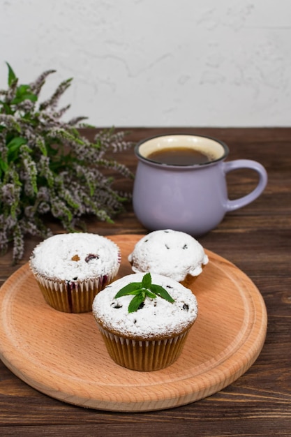 Cupcakes with black currants on a background of flowers and mint leaves on a round board on a wooden background