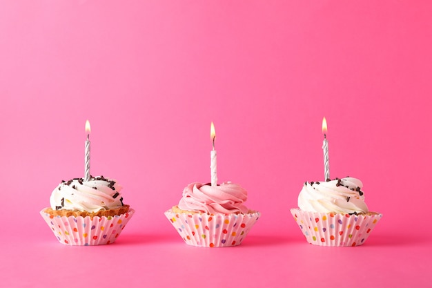 Cupcakes with candle on pink background, space for text