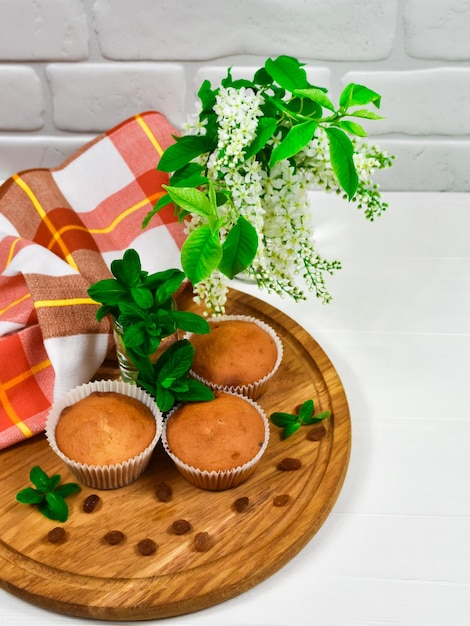 Cupcakes on a wooden board with raisins and a bouquet of white flowers Three cupcakes on a blackboard with a tablecloth and a bouquet of flowers on a white wooden table