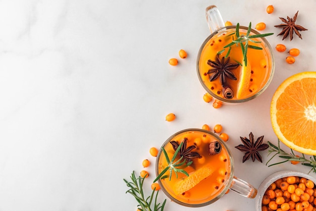 Cups of sea buckthorn tea with orange berries cinnamon and rosemary on white table healthy herbal au