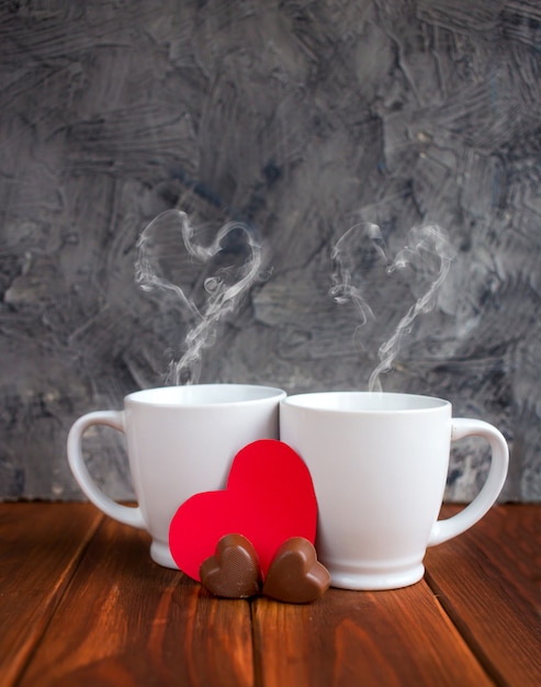 Cups of tea or coffee with steam in two heart shape on red background. Valentine's day celebration or love concept. Copy space