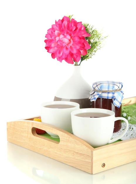 Cups of tea with flower and jam on wooden tray isolated on white