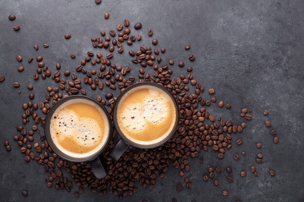 Cups with coffee and coffee beans on dark stone.