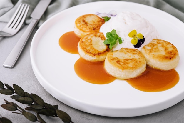 Curd pancakes with sour cream and jam on a white plate