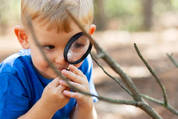 Curious boy is exploring nature with magnifying glass outdoors