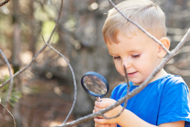 Curious boy is exploring nature with magnifying glass outdoors