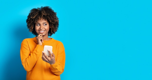 Curious excited black woman using cell phone on blue