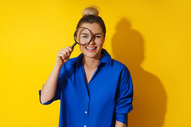 Curious woman is peering through magnifying glass with great interest examining something closely