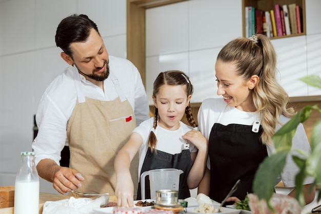 Curious young daughter showing pizza ingredients helping father and mother in modern kitchen baking