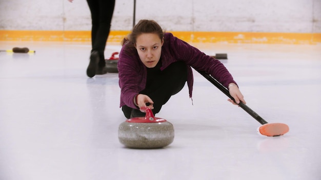 Curling  a woman skating on ice field with a granite stone holding a brush