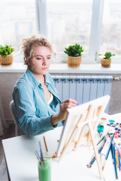 Curly blonde woman painting a picture by the window