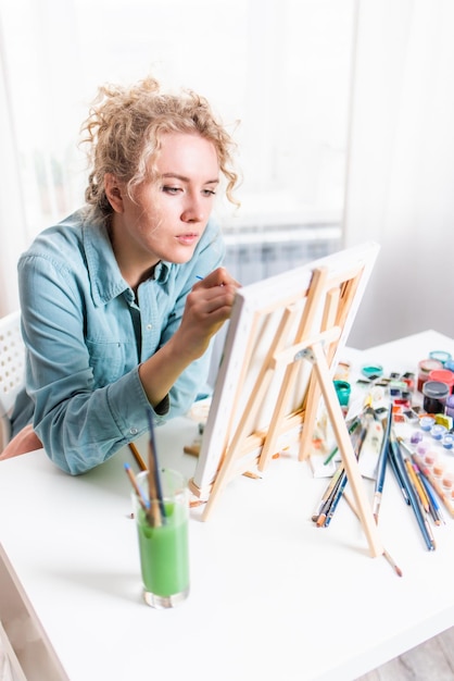 Curly blonde woman painting a picture by the window