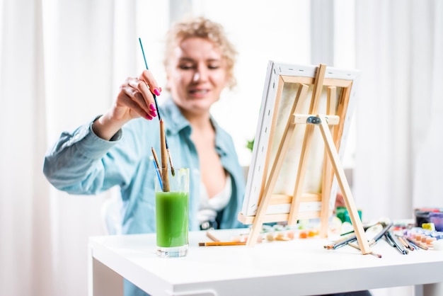 Curly blonde woman painting a picture by the window