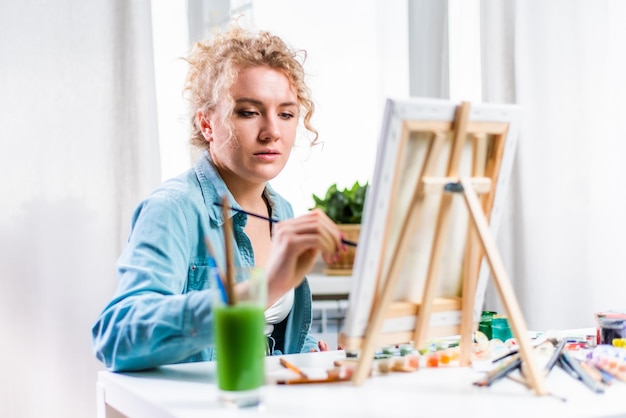 Curly blonde woman painting a picture by the window