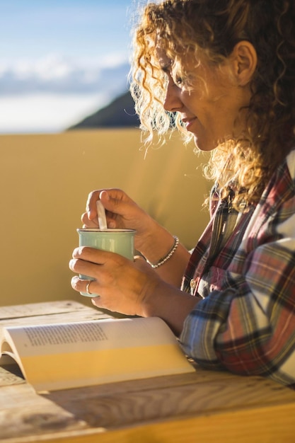 Photo curly blonde woman relaxes reading a book sitting at the table on the terrace leisure and relaxation concept