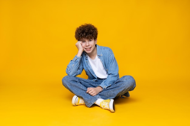 Curly boy teenager sitting on the floor on a yellow background