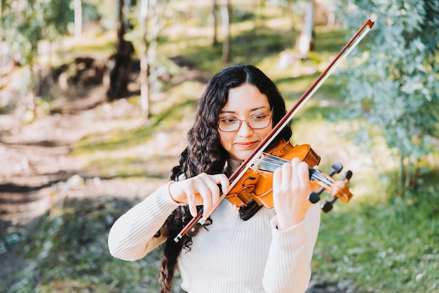 Curly brunette woman with glasses playing violin in the forest Selective focus