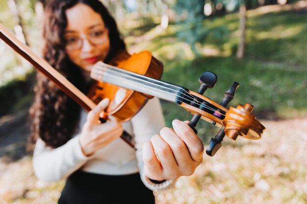 Curly brunette woman with glasses tuning her violin outside in the woods Copy space