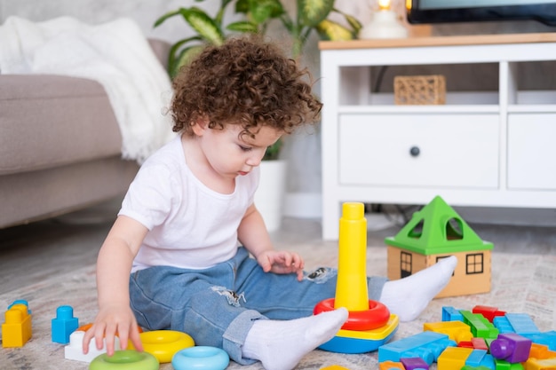 Curly child girl playing with pyramid and constructor at home early children development