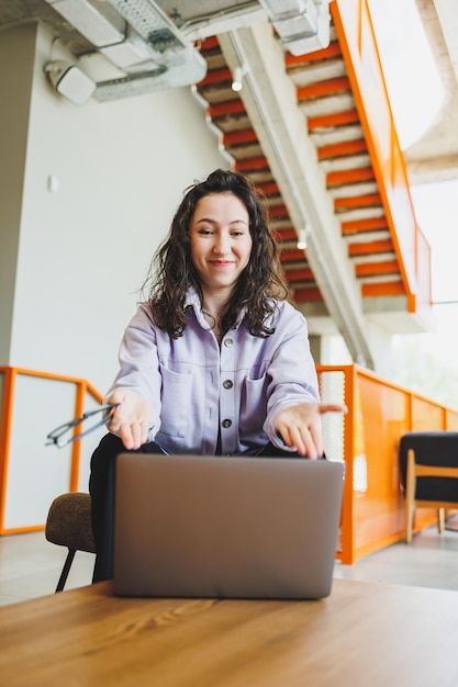 Curly female student working in bright cafe online looking at laptop Remote work with a laptop in a cozy work cafe