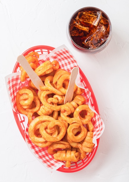 Curly fries fast food snack in red plastic tray with glass of cola on kitchen. Unhealthy junk food