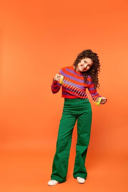 Photo curly girl poses with slinky toy on orange background