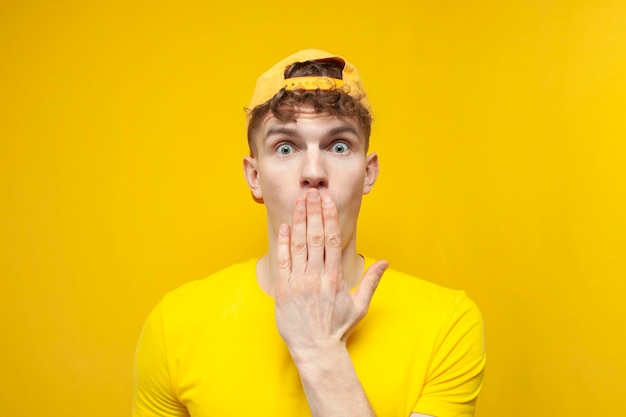 Curly guy in shock covered his mouth with his hand and wonders on a yellow background