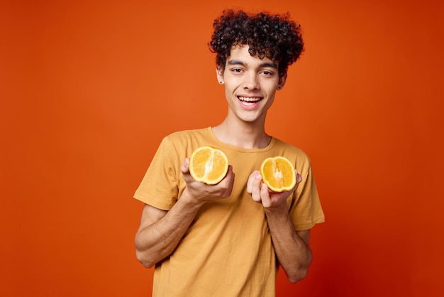 Curly guy in a yellow tshirt oranges in his hands red background