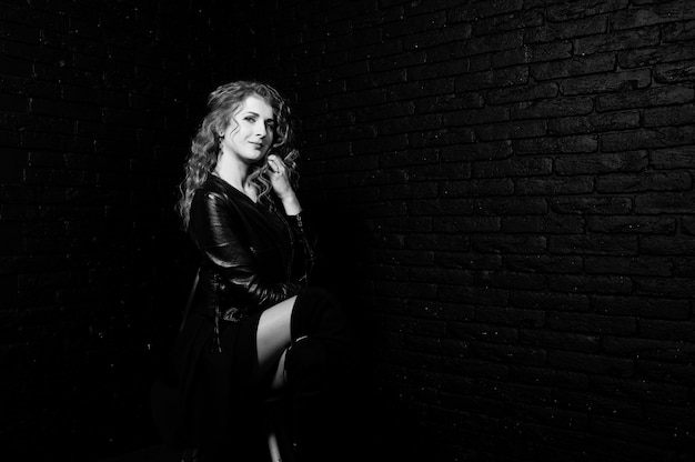 Curly hair girl at leather jacket on studio against black brick wall.