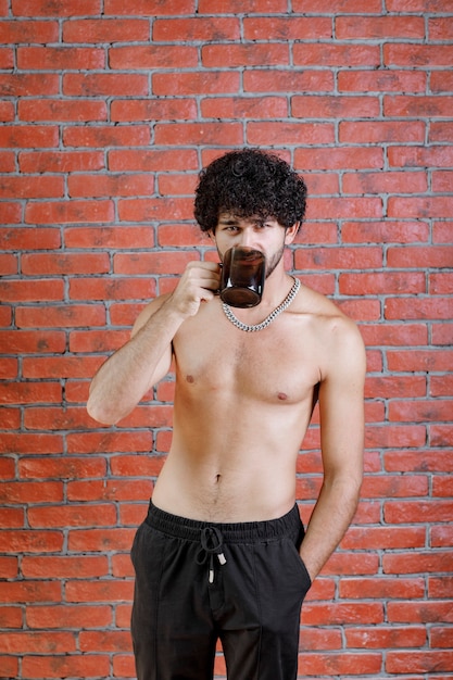 Curly haired half naked man drinkng cup of tea.