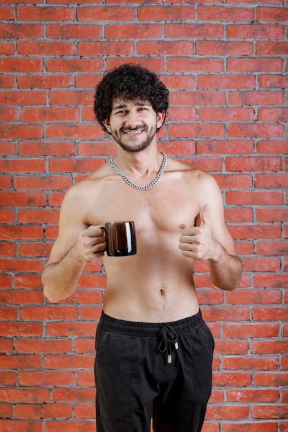 Curly haired half naked man holding cup of tea.