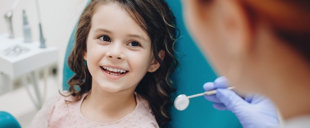 Curly haired little girl looking and smiling to the dentist after a checking up