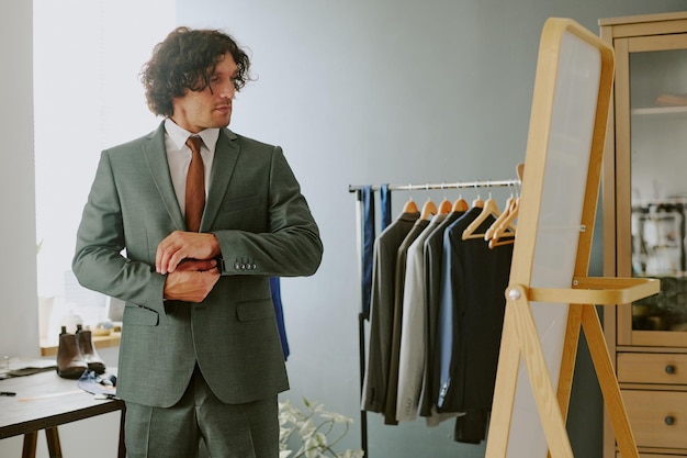 Photo curly haired male model adjusting sleeve in front of vertical mirror in atelier