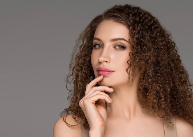 Curly long brunette hair woman touching face beauty close up female portrait. Color backgound gray