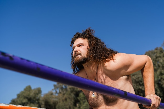 Curly man working out on parallel bars during his beach training