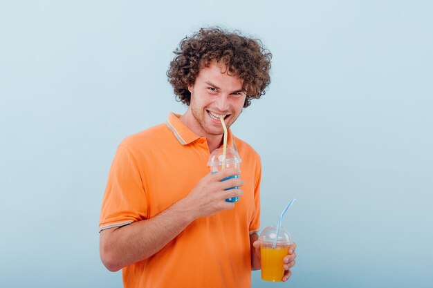 Curly modern man in bright orange t shirt drinking with straw from plastic cup 