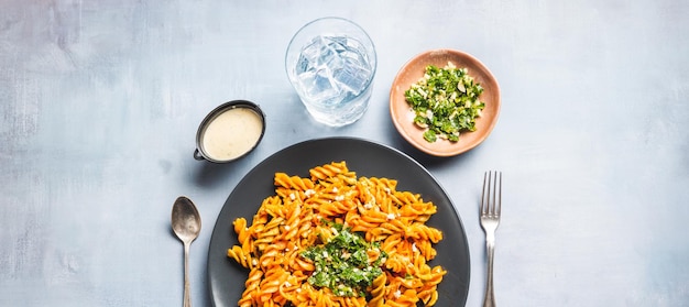 Photo curly pasta macaroni with tomato and gremolata sauce in a round dark plate on a table