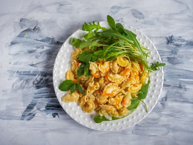 Curly pasta with vegetables basil and arugula on a white plate