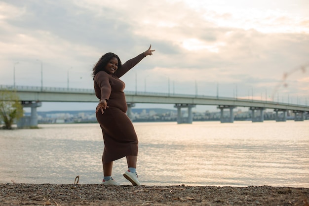 Curly smiling and playful African AfroAmerican plump blackhaired multicultural woman fooling around near river beach