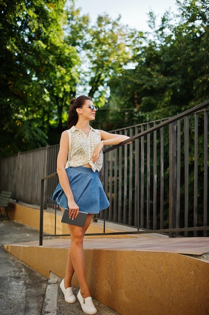 Curly stylish girl wear on blue jeans skirt blouse with tablet on hands