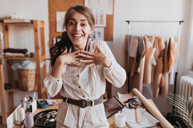 Curly woman in beige outfit happily looks at front