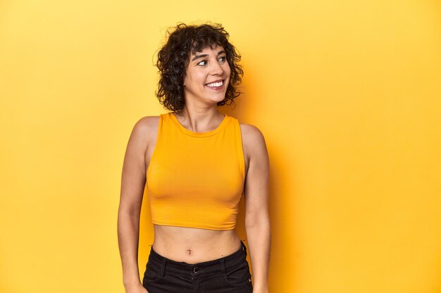 Photo curlyhaired caucasian woman in yellow top relaxed and happy laughing neck stretched showing teeth