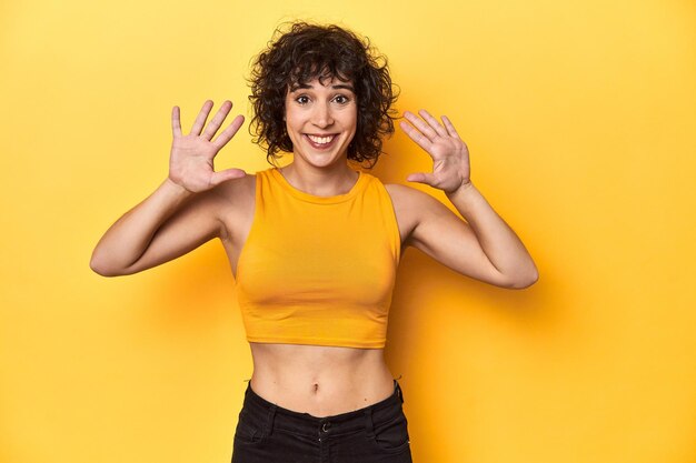 Curlyhaired Caucasian woman in yellow top showing number ten with hands