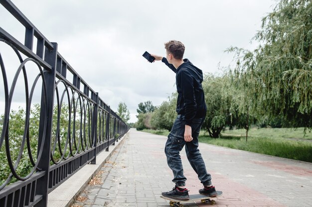 A curlyhaired teenager of european appearance in a black hoodie standing on a skateboard in an alley...