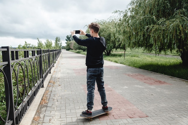 A curlyhaired teenager of european appearance in a black hoodie standing on a skateboard in an alley...