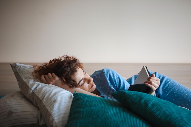 Curlyhaired woman hold book novel book at home lying on the couch relaxing and enjoying