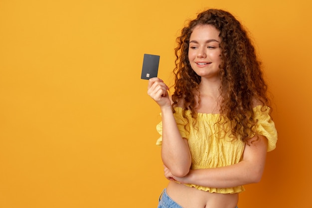 Curlyhaired woman holding black credit card against yellow background