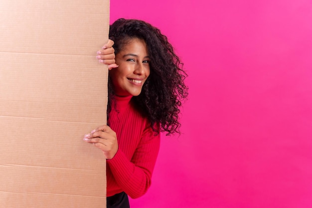 Curlyhaired woman holding a sign smiling on a pink background studio shot