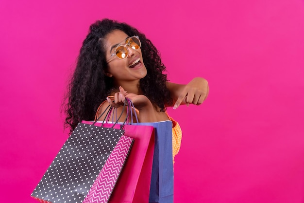 Curlyhaired woman on a pink background shopping concept pointing at the paper bags studio shot